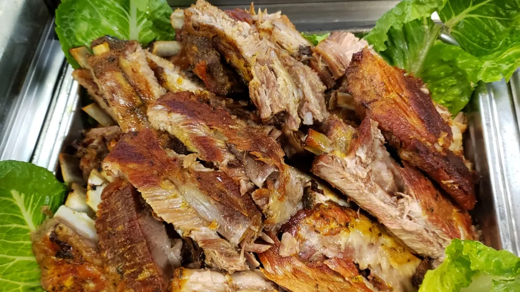 Roast pork pieces with browned, crisp edges on romaine lettuce in a steel tray