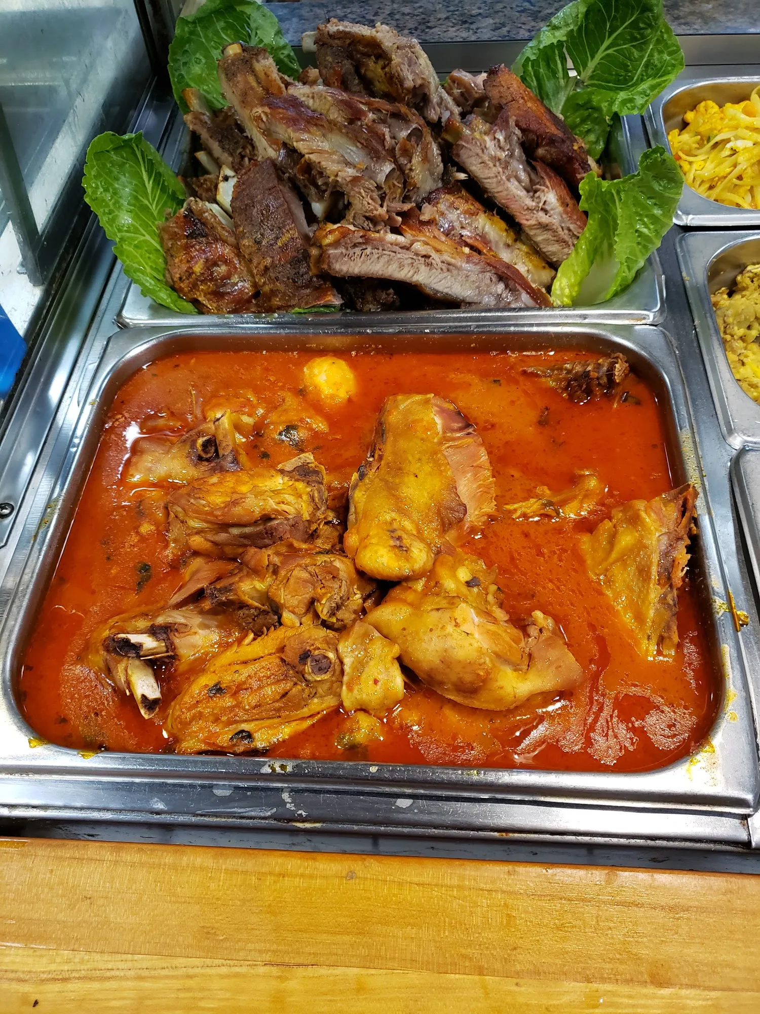 Roast pork on romaine above a tray of chicken pieces in red sauce on the steam table
