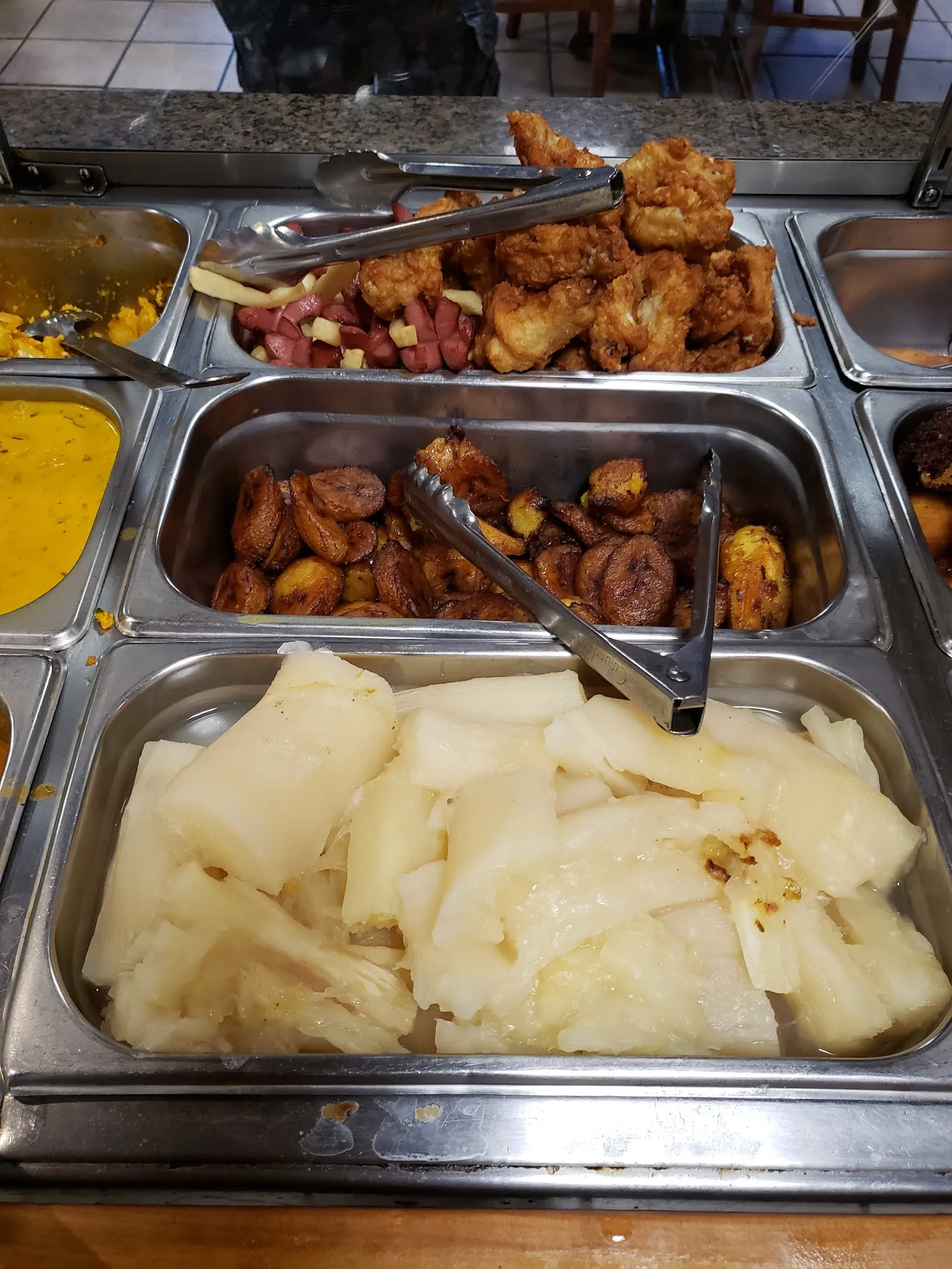 Steam table trays of boiled yuca, sweet plantains and fried pork pieces
